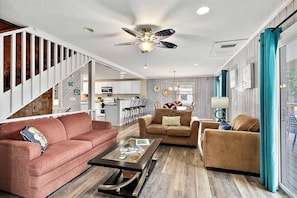 A spacious living room with a staircase, a ceiling fan, and a view to the outside. - Happy Daze Home, Fire Pit, Gazebo & Vilano Pier (St. Augustine)