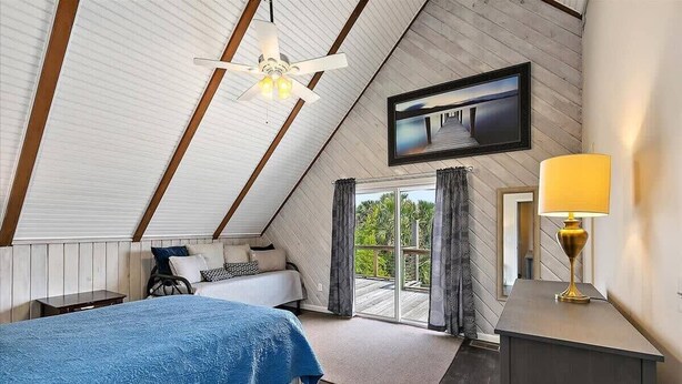 Une chambre à coucher avec un lit, un ventilateur de plafond, une télévision et une vue sur l’extérieur.