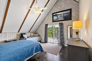 Ein Schlafzimmer mit einem Bett, einem Nachttisch, einer Lampe, einem Deckenventilator und einem großen Fenster mit Vorhängen.