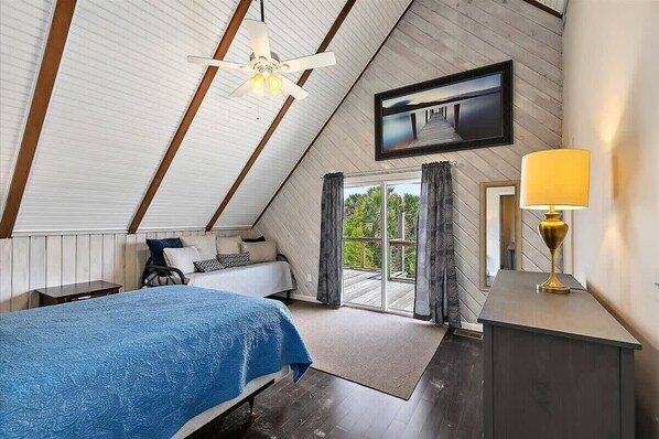 A bedroom with a bed, a nightstand, a lamp, a ceiling fan, and a large window with curtains.