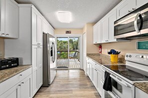 A kitchen with white cabinets, a stainless steel refrigerator, a microwave, and a stove. - Happy Daze Home, Fire Pit, Gazebo & Vilano Pier (St. Augustine)
