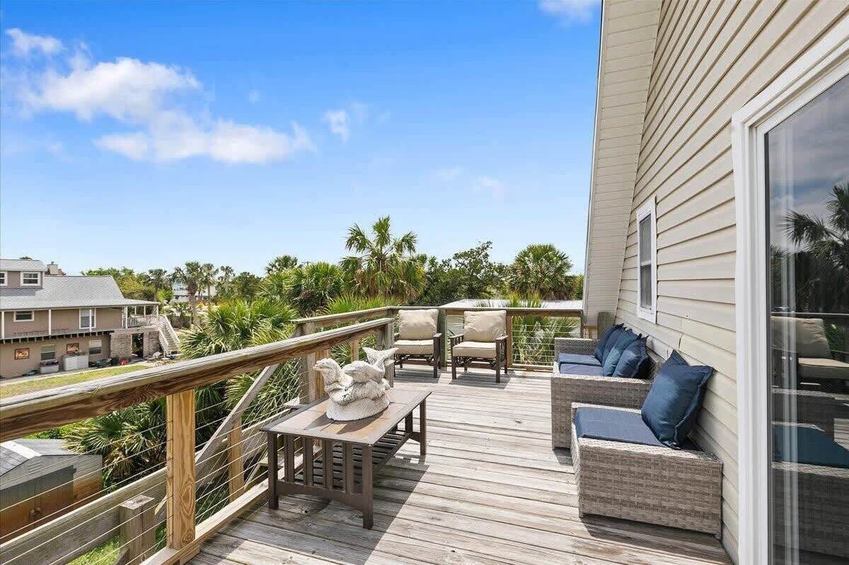 Une terrasse en bois, aménagée avec du mobilier d’extérieur, notamment un canapé et des fauteuils, qui offre une vue sur un quartier résidentiel bordé de palmiers et de maisons.
