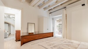Une chambre avec un lit en bois, une armoire blanche, un miroir et une vue sur l’extérieur par une fenêtre ornée de rideaux.