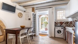 Une cuisine compacte équipée d’un lave-linge, un coin repas avec une table et des chaises, et une grande fenêtre donnant sur l’extérieur.
