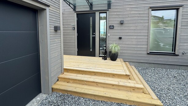 A modern building with a grey exterior, a black garage door, and a wooden staircase leading to the entrance. - Ny og Moderne Studio- Leilighet ved Fetsund i Lillestrøm (Akershus)
