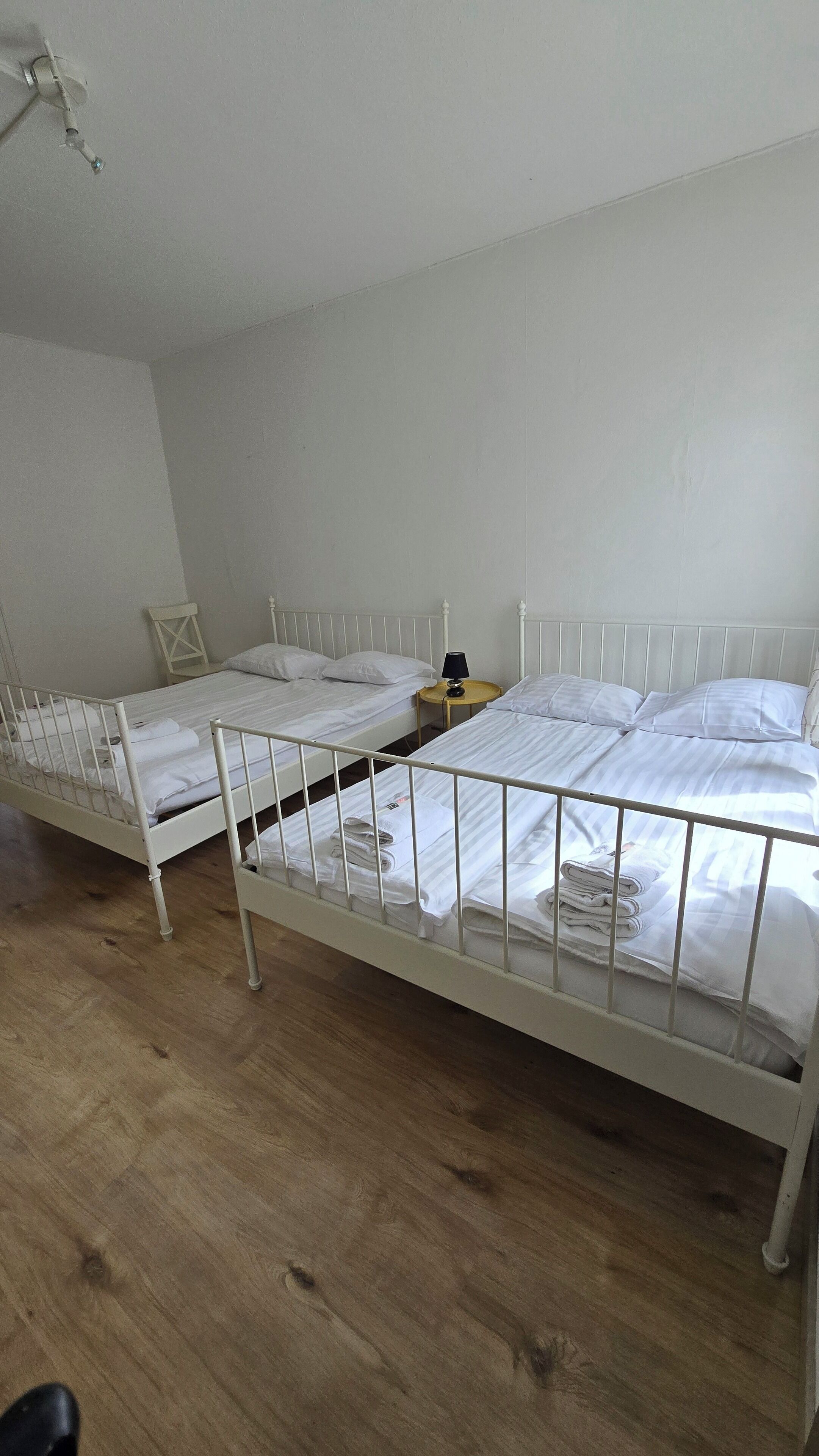 A room with two single beds, a small table with a lamp, and a wooden floor.