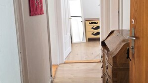 A hallway with wooden flooring, a red curtain, a wooden dresser, and a door with a number plaque. - Mi Casa es su Casa (Zürich)