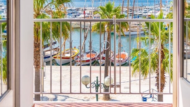 Een balkon met uitzicht op een jachthaven, palmbomen en boten.