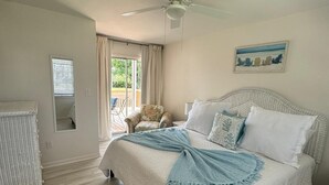 Un dormitorio con cama, ventilador de techo, ventana con cortinas y una silla junto a la ventana.