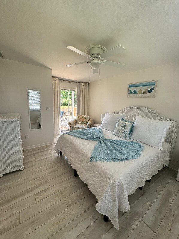 A bedroom with a bed, a ceiling fan, a window with curtains, and a chair by the window.