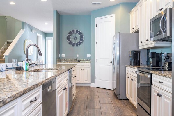 A kitchen with white cabinets, a stainless steel refrigerator, a microwave, and a clock on the wall. - Luxury 9BR Villa - Private Pool, Spa, Game Room - Free Pool Heat in Aug - Oct! (Kissimmee)
