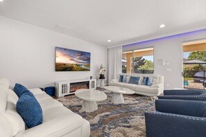 A modern living room with a fireplace, white sofas, a coffee table, and a large window overlooking a garden.