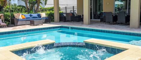 Une piscine avec un jacuzzi, entourée de mobilier d’extérieur et d’un espace salon abrité.