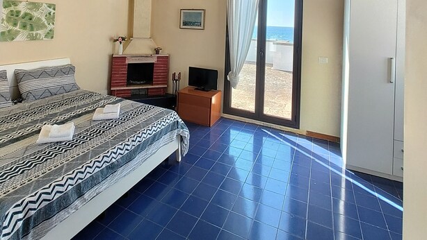 Een hotelkamer met een bed, een televisie, een open haard en uitzicht op het strand door een schuifdeur.
