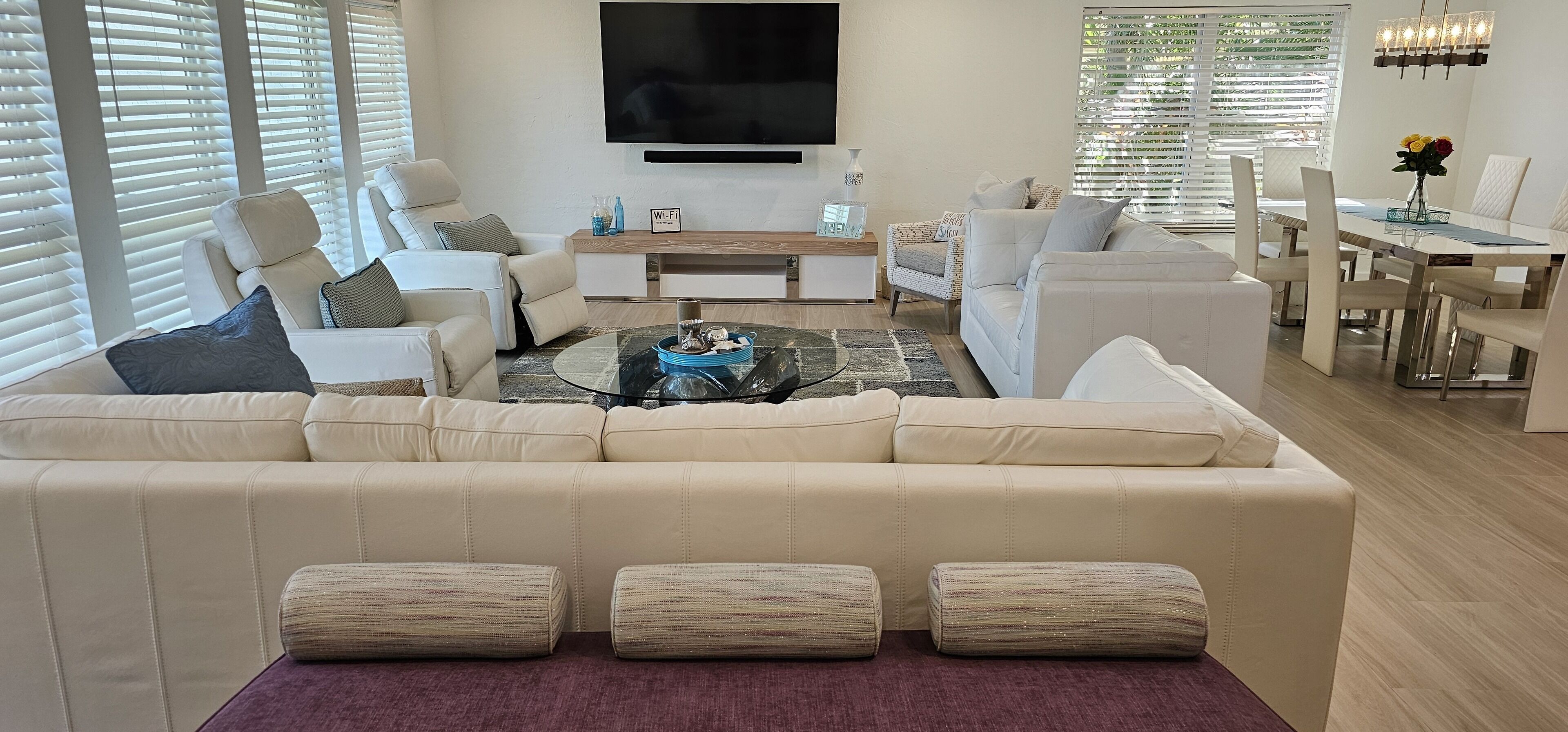 En moderne stue med en beige hjørnesofa, et sofabord i glas, samt et spiseområde med et hvidt bord og stole.
