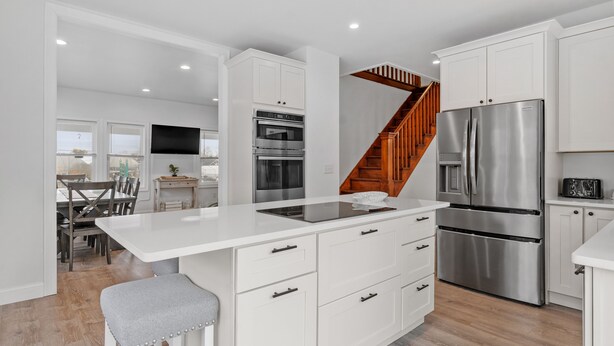 Una cocina moderna con armarios blancos, electrodomésticos de acero inoxidable, una isla central y una escalera de madera.