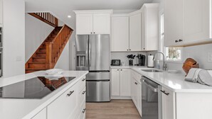 Una cocina moderna con armarios blancos, electrodomésticos de acero inoxidable, horno empotrado y una escalera de madera.