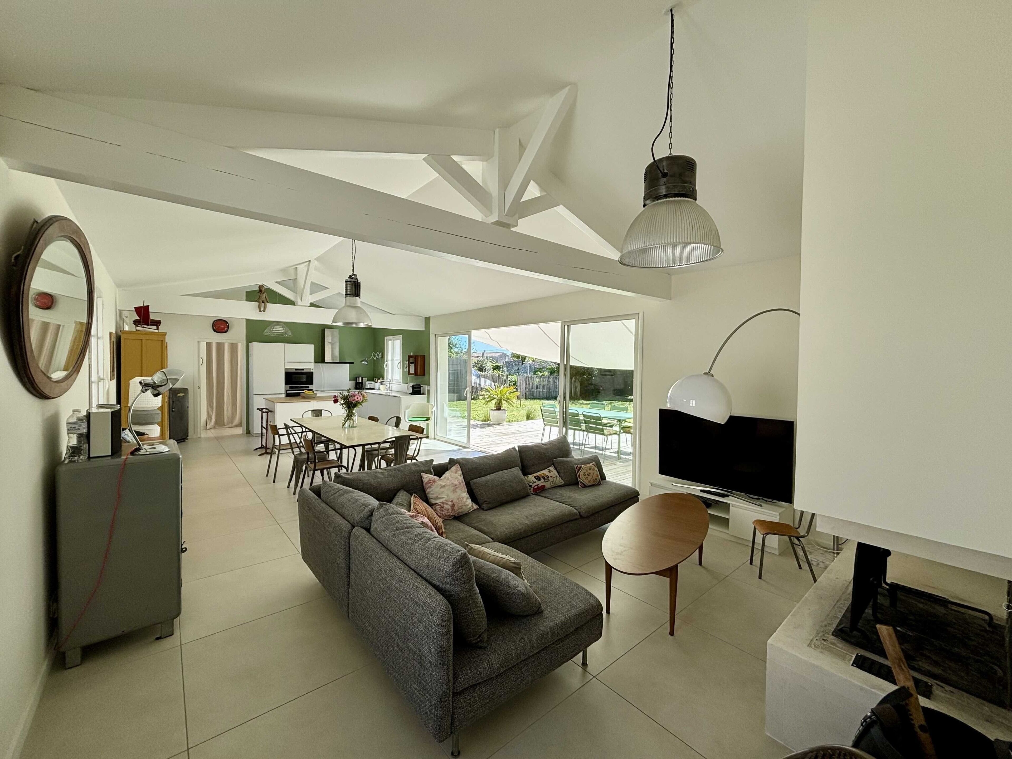 A modern living room with a grey sofa, a dining area, and a kitchen.