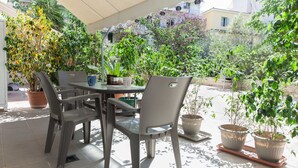 An outdoor patio with a table and chairs, surrounded by potted plants and a view of buildings in the background. - Modern 2 Bd Kipseli Hideaway Patio Apt (Athens)