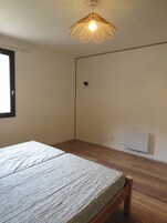 Un dormitorio con cama, suelo de madera, radiador blanco y lámpara colgante.