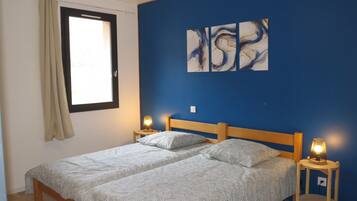 Une chambre à coucher avec un lit double, deux lampes de chevet, une fenêtre avec des rideaux et des œuvres d’art abstraites accrochées au mur.