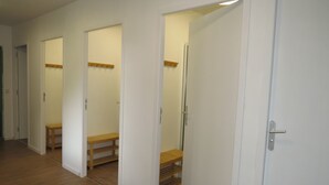Un pasillo con paredes blancas y suelo de madera. Hay tres puertas, cada una que da a una habitación diferente. Las puertas tienen pomos de madera y una de ellas tiene un espejo encima.