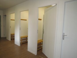 Un pasillo con paredes blancas y suelo de madera. Hay tres puertas, cada una que da a una habitación diferente. Las puertas tienen pomos de madera y una de ellas tiene un espejo encima.