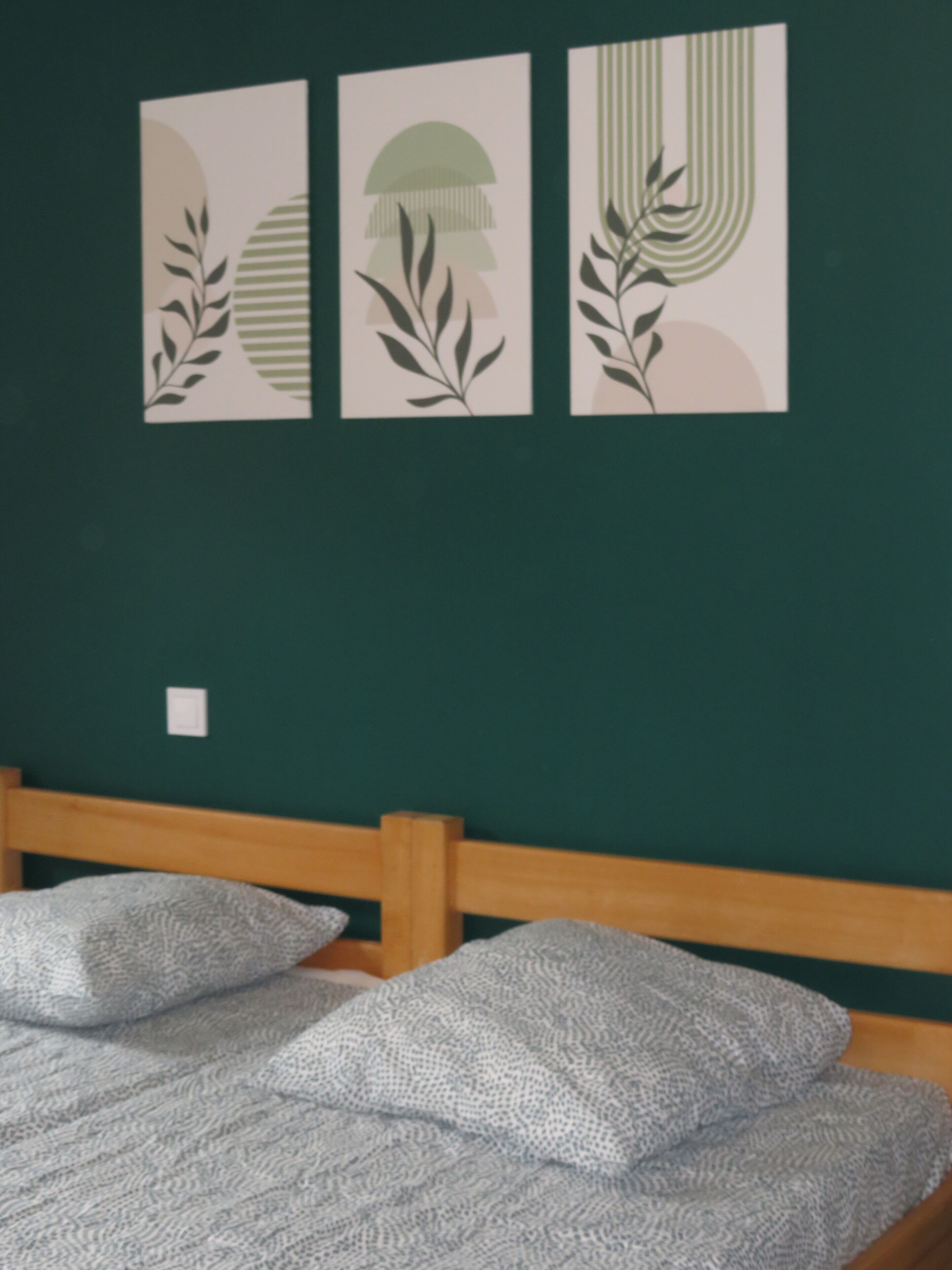 Una habitación con una cama, una pared verde y tres cuadros enmarcados.