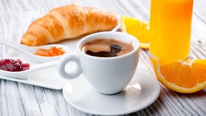 Un desayuno con un croissant, una taza de café, un vaso de jugo de naranja y una cuchara con mermelada.