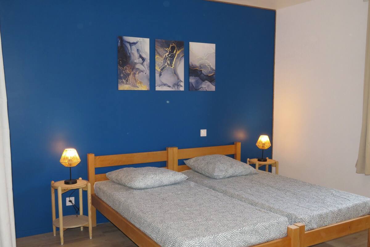A bedroom with a wooden bed, two bedside lamps, and three abstract paintings on the wall.