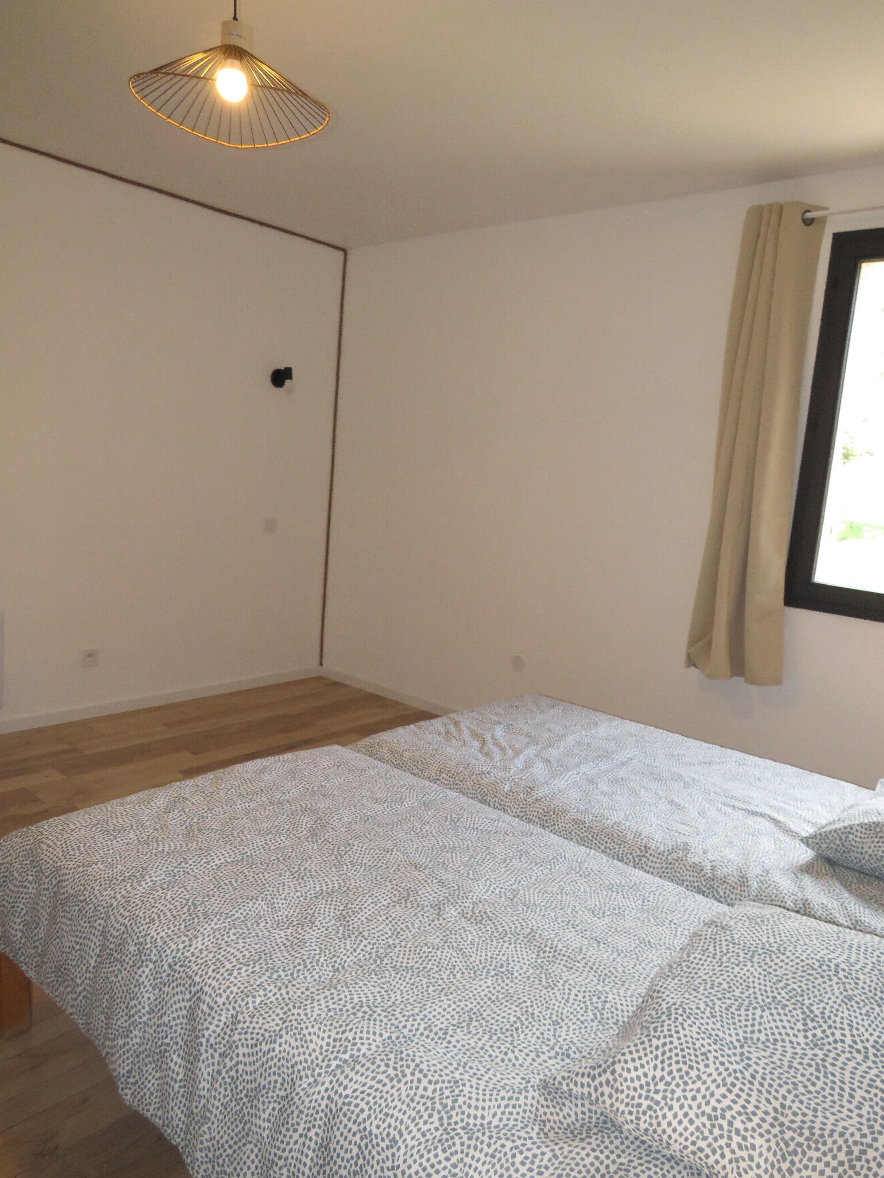 Una habitación con cama, lámpara colgante, ventana con cortinas y una puerta.