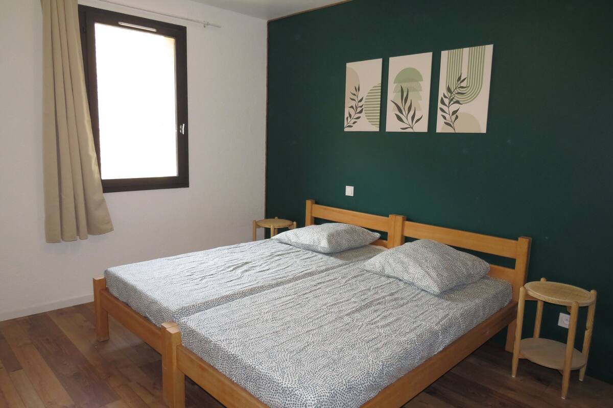 A bedroom with a wooden bed, a small bedside table, a window with curtains, and three wall art pieces.
