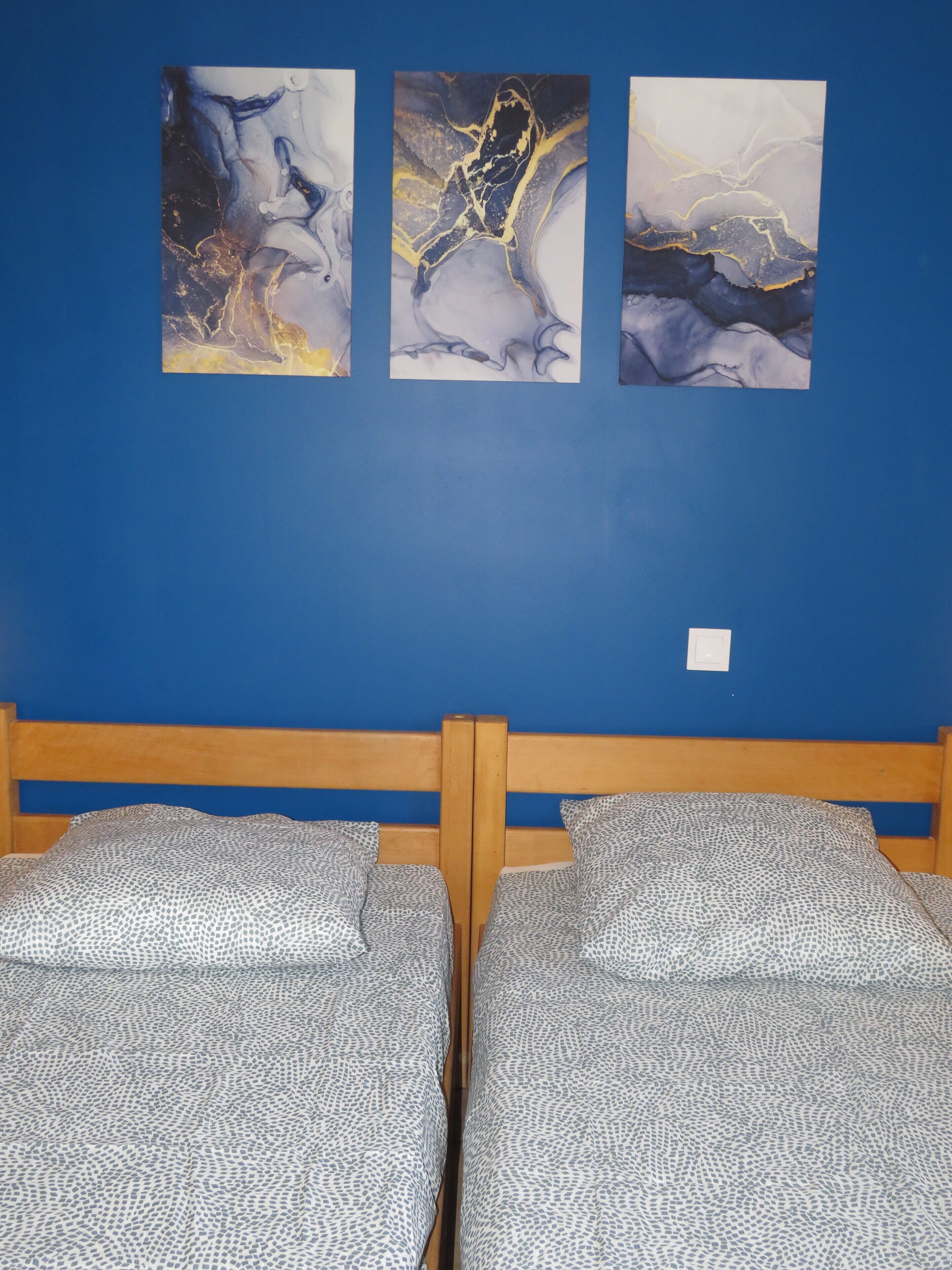 Ein Zimmer mit zwei Betten, einer blauen Wand und drei abstrakten Bildern.