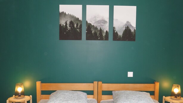 Una habitación con dos camas, una pared verde y tres cuadros enmarcados con paisajes de montañas.