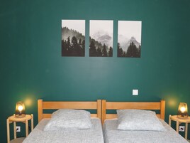 Una habitación con dos camas, una pared verde y tres cuadros enmarcados con paisajes de montañas.