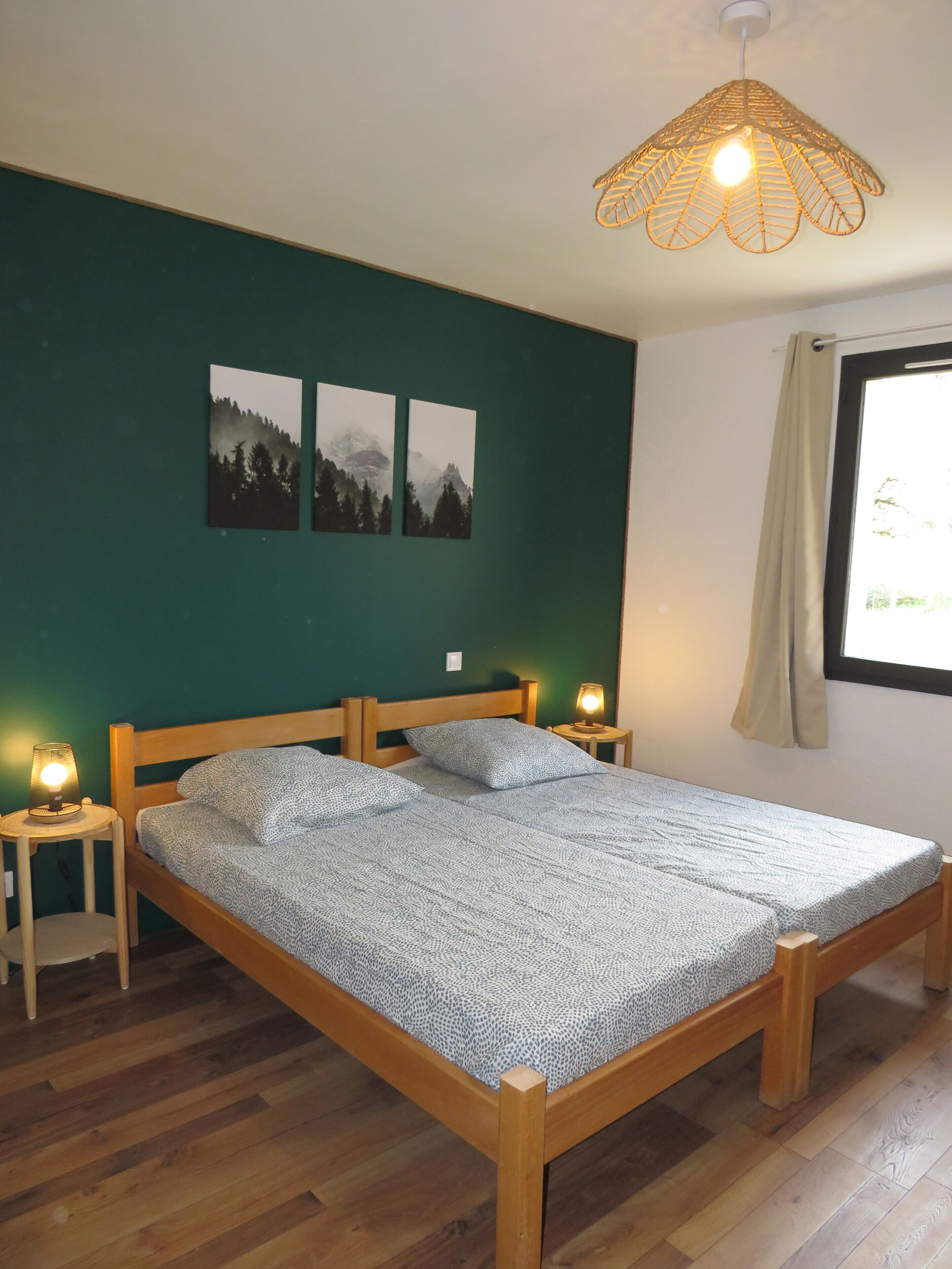 Une chambre à coucher avec un lit en bois, deux tables de chevet, un mur vert et une fenêtre avec un rideau.