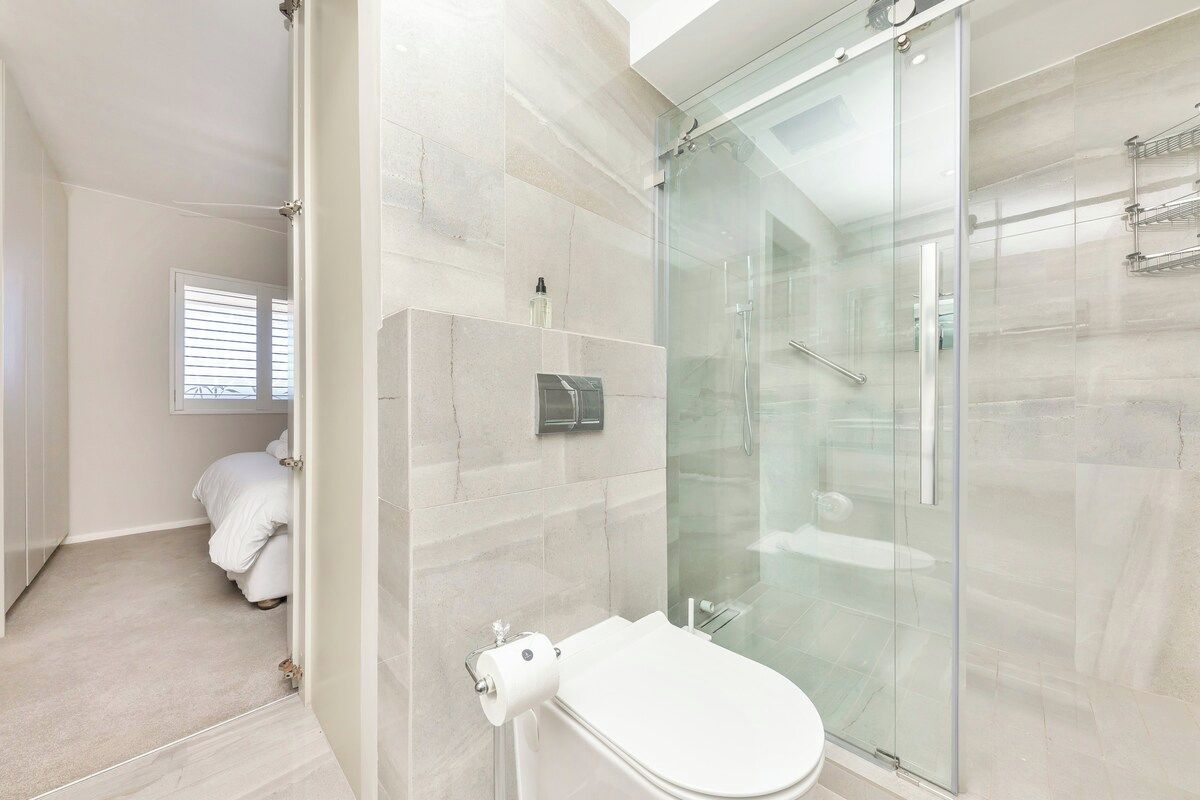 A modern bathroom with a glass-enclosed shower, a toilet, and a towel rack.