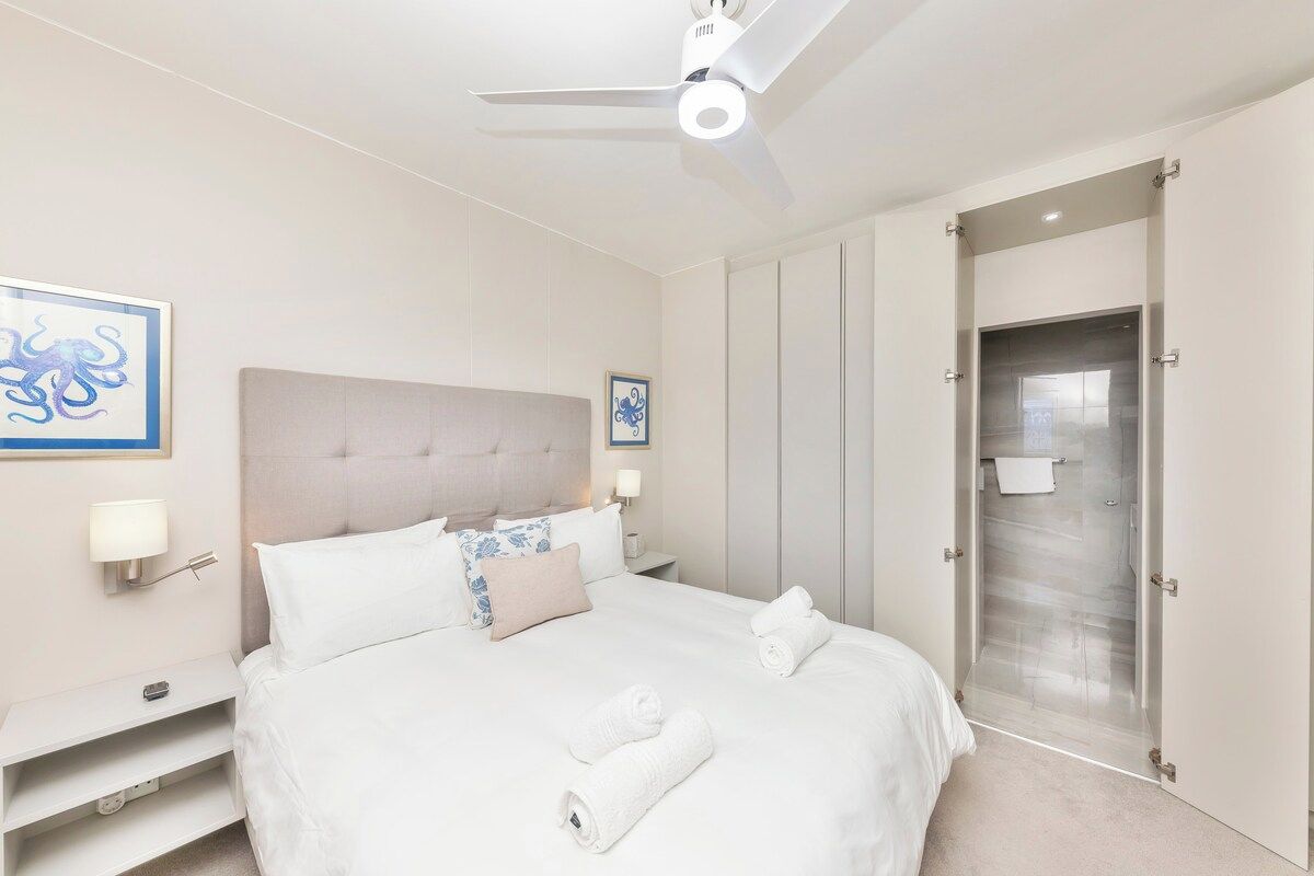 A hotel room with a bed, a nightstand, a ceiling fan, and a door leading to a bathroom.