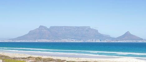 Un paysage côtier avec une montagne imposante en arrière-plan, une plage au premier plan et une vue sur la ville de l’autre côté de l’eau.