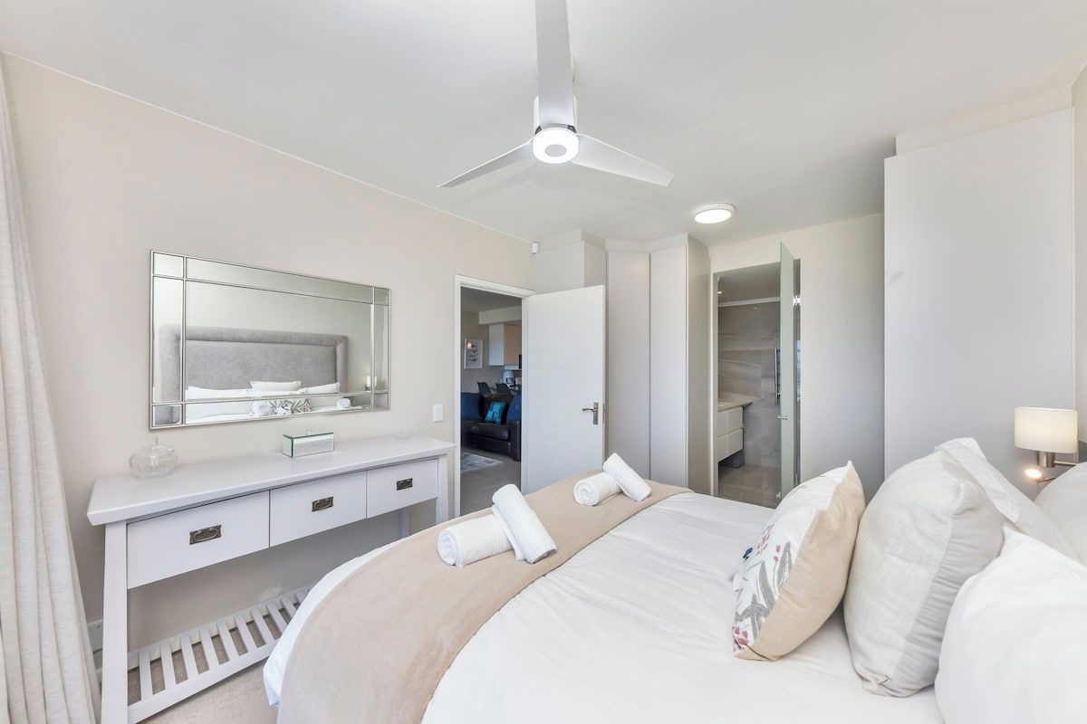Une chambre d’hôtel comprenant un lit, une coiffeuse avec un miroir, un ventilateur de plafond et un dressing.