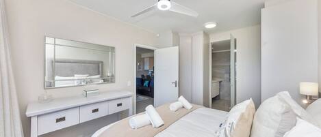 Habitación de hotel con cama, tocador con espejo, ventilador de techo y vestidor.