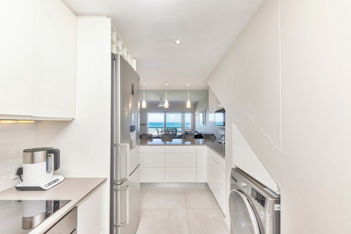 A modern kitchen with a built-in washing machine, a coffee maker, and a view of the ocean.