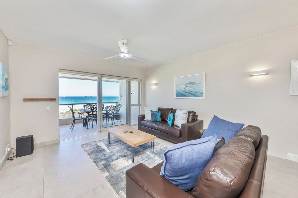 A modern living room with a sofa, coffee table, and a view of the sea through a sliding glass door.