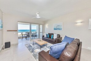 Ein modernes Wohnzimmer mit einer Couch, einem Couchtisch und Blick auf das Meer durch eine Schiebetür.