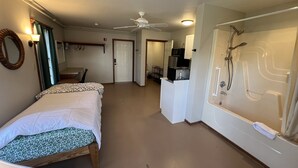 A hotel room with a bed, a desk, a microwave, and a shower.