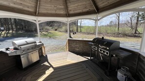 An outdoor gazebo with a wooden deck, two barbecue grills, and a propane tank.