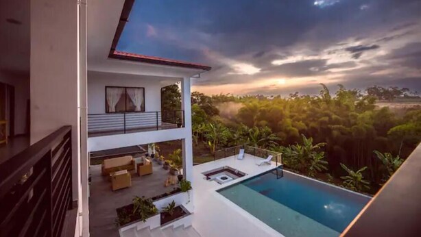 Ein modernes, zweistöckiges Gebäude mit Pool auf dem Dach und einem Balkon mit Blick auf eine üppige Landschaft.