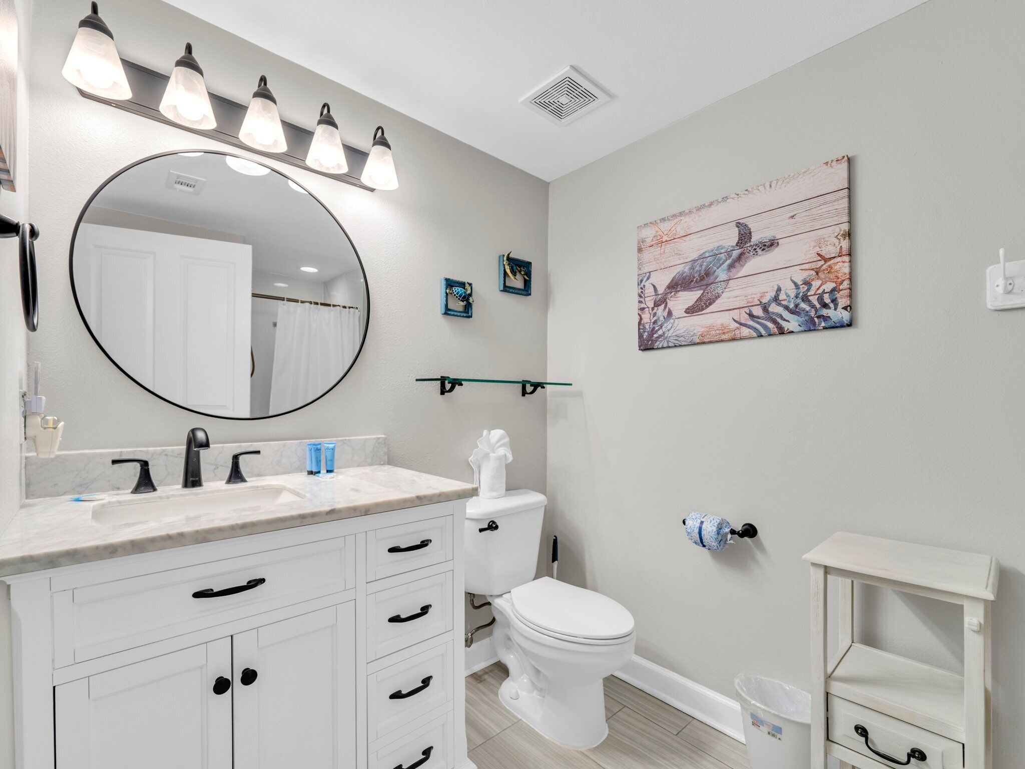 A bathroom with a white vanity, a round mirror, a toilet, and a shower curtain.