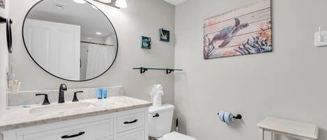 A bathroom with a white vanity, a round mirror, a toilet, and a shower curtain.