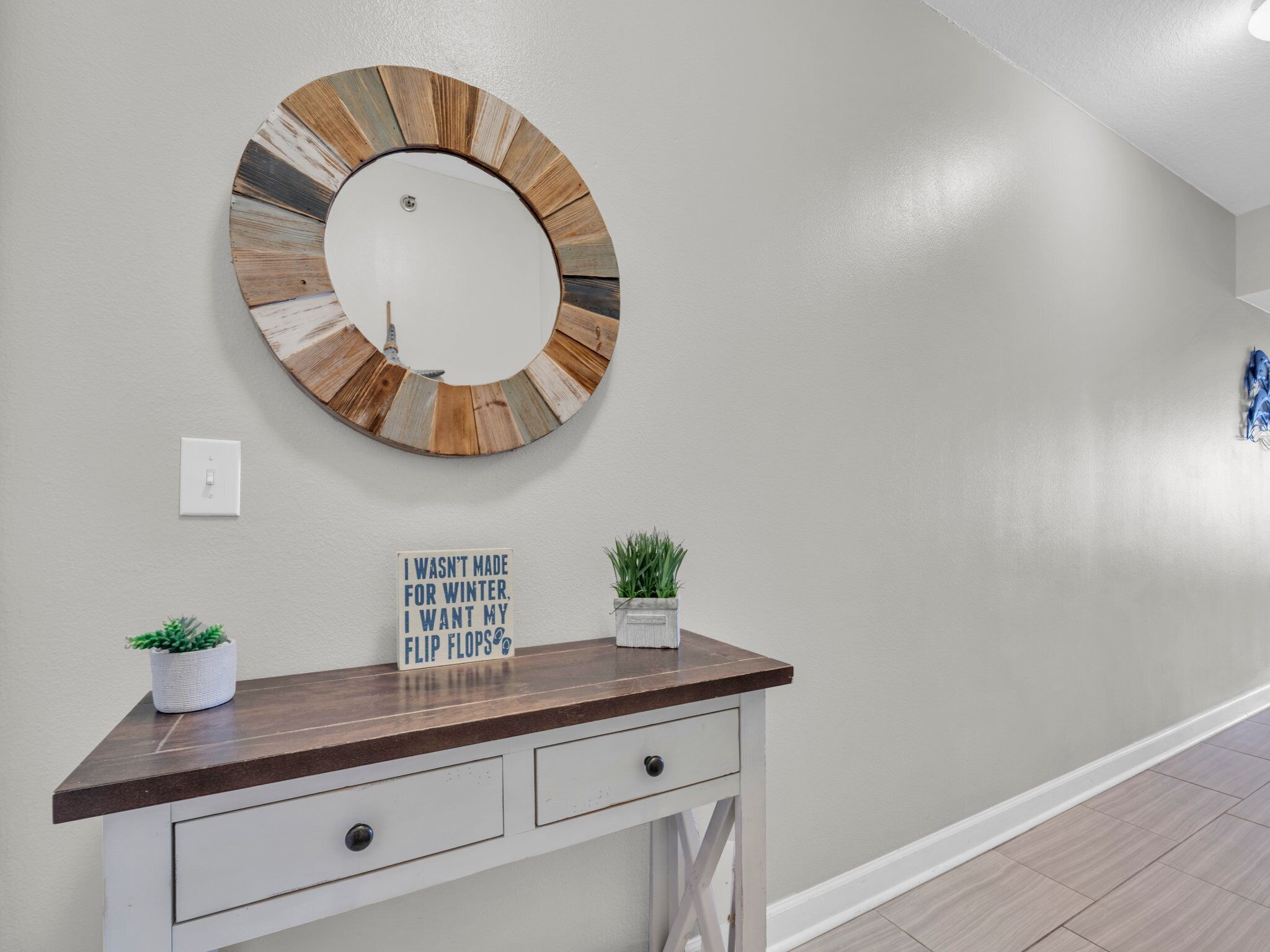 A hallway with a round mirror, a sign with a quote, a small plant, and a wooden desk with drawers.